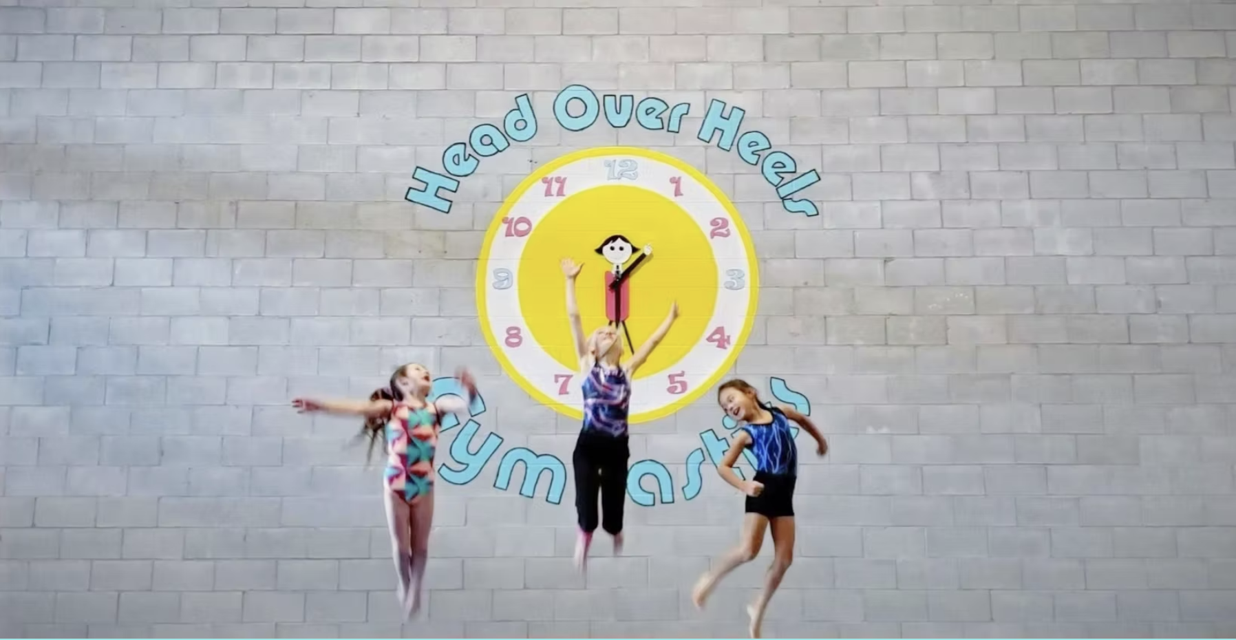 2 children jumping in front of the Head Over Heels Logo Clock